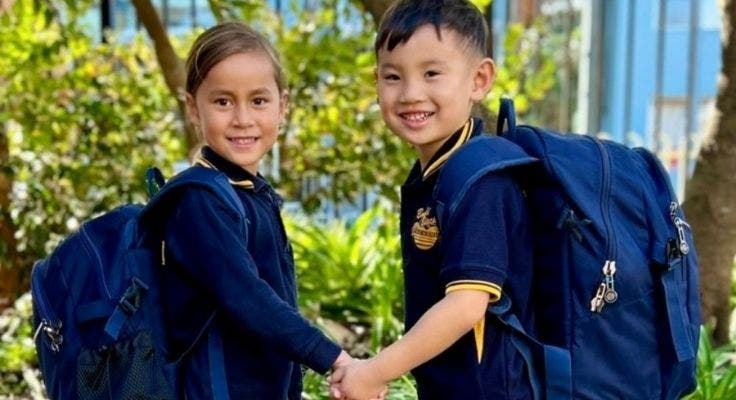 Photo of two students holding hands, wearing full school uniform.